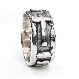 Puede incluir: Un anillo de plata con un diseño geométrico texturizado. El anillo presenta una forma de cruz en relieve.