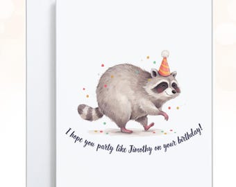 May include: A white greeting card featuring a watercolor illustration of a grey raccoon wearing a striped orange and pink party hat. The raccoon is surrounded by colorful confetti dots. The text reads, I hope you party like Timothy on your birthday!