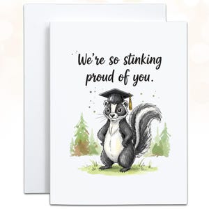 May include: A white graduation card with a watercolor illustration of a skunk wearing a graduation cap. The card reads, "We're so stinking proud of you." The skunk stands in front of a green and brown forest scene.