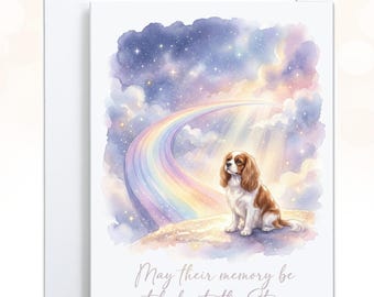 May include: A white greeting card featuring a watercolor illustration of a brown and white Cavalier King Charles Spaniel sitting on a hill under a rainbow and a starry night sky. The text reads, May their memory be etched into the Stars.