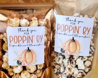 May include: Two stand-up pouches filled with popcorn, featuring labels that read Thank you FOR POPPIN' BY to sprinkle our little pumpkin! with a watercolor pumpkin illustration. The left bag is metallic gold, and the right bag is clear plastic.