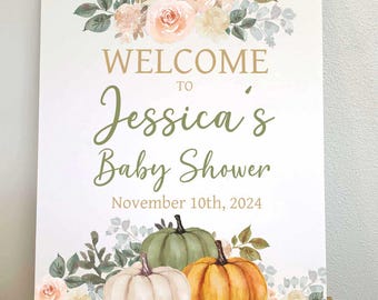 May include: A baby shower welcome sign with floral and pumpkin illustrations. The sign reads "WELCOME to Jessica's Baby Shower November 10th, 2024". The design features peach and cream-coloured flowers and three pumpkins.