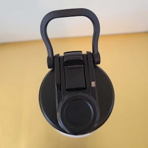 May include: A black water bottle lid with a built-in handle. The lid has a flip-top closure and a round, black cap. The handle is curved for easy carrying. The bottle is likely designed for sports or outdoor activities.
