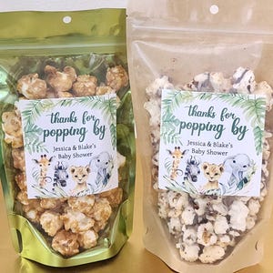 May include: Two clear cellophane bags filled with popcorn. One bag has caramel popcorn, the other has white popcorn. Each bag has a label that reads "thanks for popping by" with baby animal illustrations and "Jessica & Blake's Baby Shower."