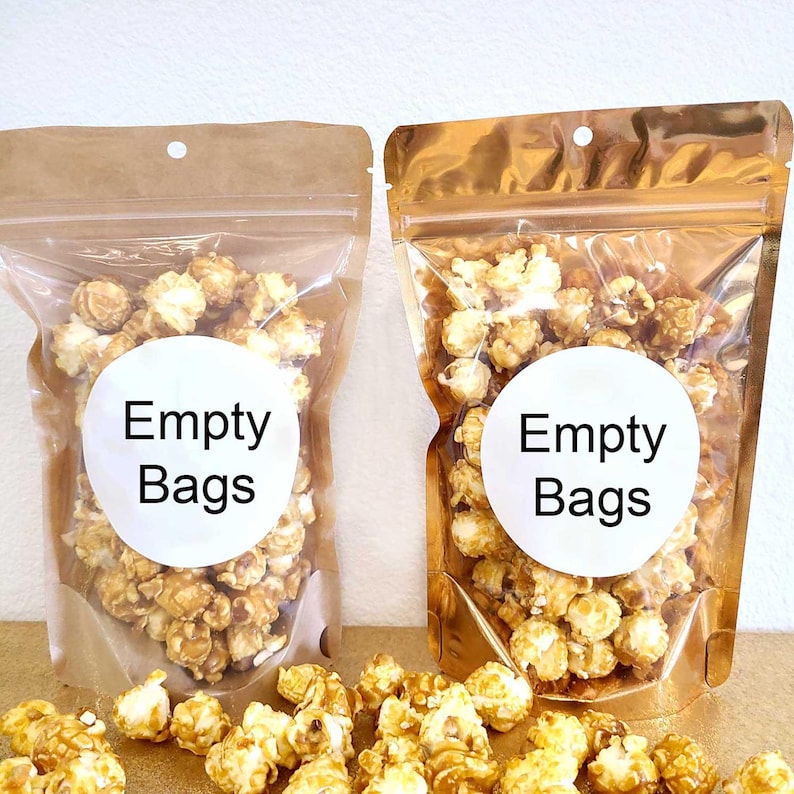 Puede incluir: Dos bolsas vac&iacute;as para palomitas de ma&iacute;z, una marr&oacute;n y otra dorada, con el texto "Empty Bags" en una etiqueta circular blanca. Las bolsas est&aacute;n llenas de palomitas de ma&iacute;z con caramelo.