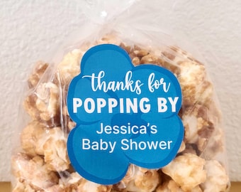 May include: A clear cellophane bag filled with caramel popcorn. A blue cloud-shaped sticker on the bag reads "thanks for POPPING BY Jessica's Baby Shower" in white script and block letters.