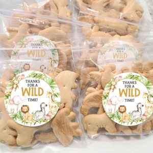 Puede incluir: Un conjunto de cuatro bolsas de plástico transparentes llenas de galletas de animales y decoradas con pegatinas redondas y coloridas que dicen "¡Gracias por un momento salvaje!"