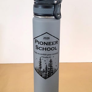 May include: A grey water bottle with a black lid and a black graphic. The graphic includes the text "2026 Pioneer School" above a forest scene and the quote "Fully accomplish your ministry" from 2 Timothy 4:5.