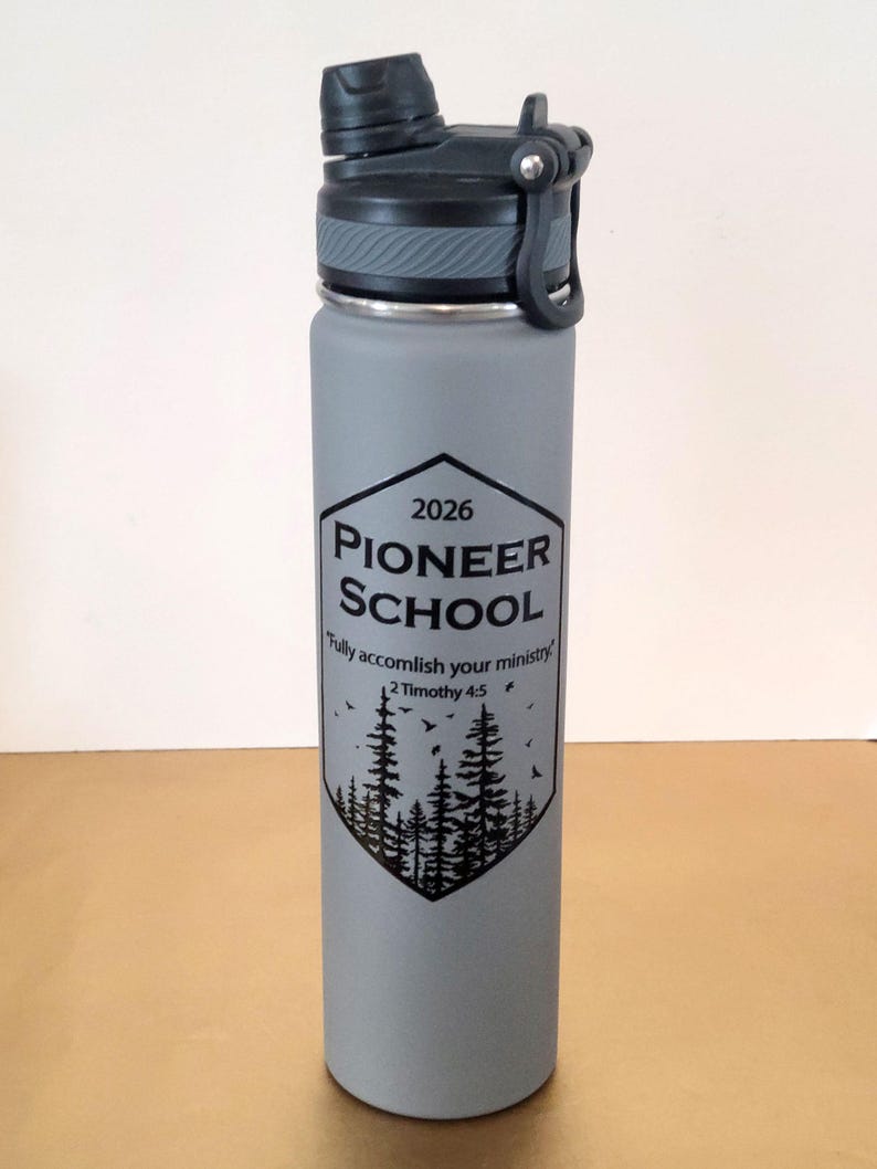 May include: A grey water bottle with a black lid and a black graphic. The graphic includes the text "2026 Pioneer School" above a forest scene and the quote "Fully accomplish your ministry" from 2 Timothy 4:5.