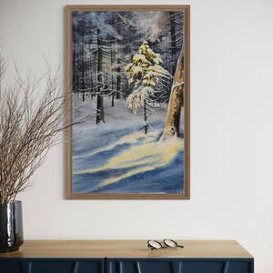 May include: A framed watercolor painting of a snowy forest scene. The artwork depicts a winter landscape with snow-covered trees and a soft, diffused light. The frame is a light brown color.