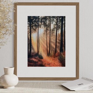 May include: A framed watercolor painting of a forest path with sunlight streaming through the trees. The path is lined with trees and the ground is covered in fallen leaves.