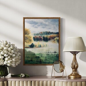 May include: A framed watercolor landscape painting depicts a misty field and trees in autumn colors. The painting is in a wooden frame and hangs above a decorative table with a lamp, mirror, and a vase of white flowers.