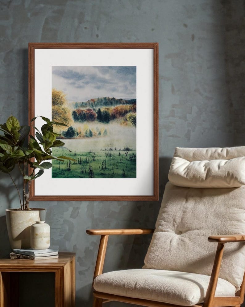 May include: A framed landscape painting depicts a misty meadow with trees in autumn colors. The artwork is in a brown wooden frame, hanging on a textured gray wall. A potted plant and a chair are in the foreground.