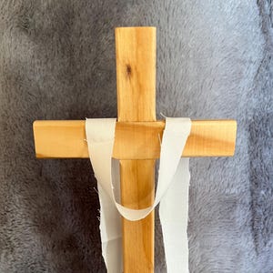 May include: A wooden cross with a white fabric tied around it. The cross is standing on a wooden base.