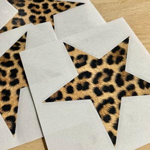 May include: Four white star-shaped cutouts with a leopard print design inside. The cutouts are layered on top of each other.