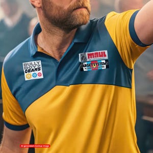 May include: A yellow and blue polo shirt featuring a collar and short sleeves. The chest displays two logos: one reads Bully Boyz Gears with three gear icons, and the other reads Maul Entertainment and Target Systems Plumbing & Heating.