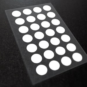May include: A clear sheet with 25 white circles arranged in a grid pattern. The circles are evenly spaced and are all the same size.