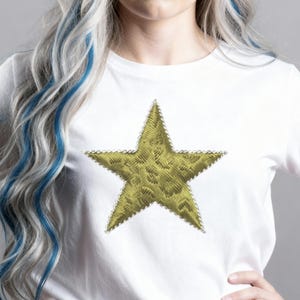 May include: White t-shirt with a large, embroidered gold star. The star has a textured pattern and is edged with small, silver beads. The shirt is a simple, casual style.