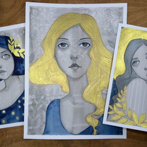 May include: Three watercolor paintings of women with gold accents. Each woman has a different hairstyle and is wearing a different color dress. The paintings are set against a background of white with gold flecks.