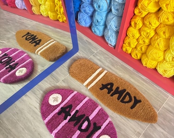 May include: Two oval-shaped doormats with the word "ANDY" written in black lettering. One doormat is brown with white stripes and the other is purple with white stripes. Both doormats have a white star in each corner.