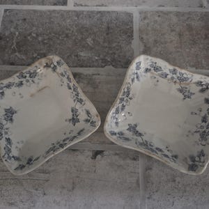 Puede incluir: Dos fuentes antiguas de servir, de forma cuadrada. Las fuentes son blancas con un estampado floral azul en los bordes. Los bordes tienen una forma ondulada única. Las fuentes están sobre una superficie gris, similar a la piedra.