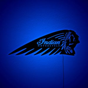 May include: Black metal wall art featuring the Indian Motorcycle logo, illuminated with blue LED lights. The design includes the iconic headdress and wing, with the words "Indian MOTORCYCLE" in a stylized font. The art is mounted on a blue wall.