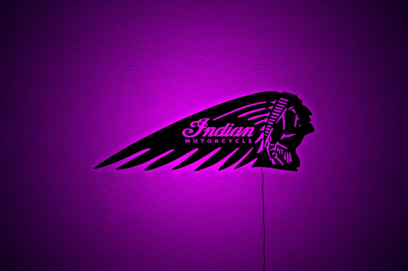 May include: Black metal Indian Motorcycle logo with a feather design, illuminated by a purple light. The logo includes the text "Indian MOTORCYCLE" in a cursive font. The image is set against a purple background.