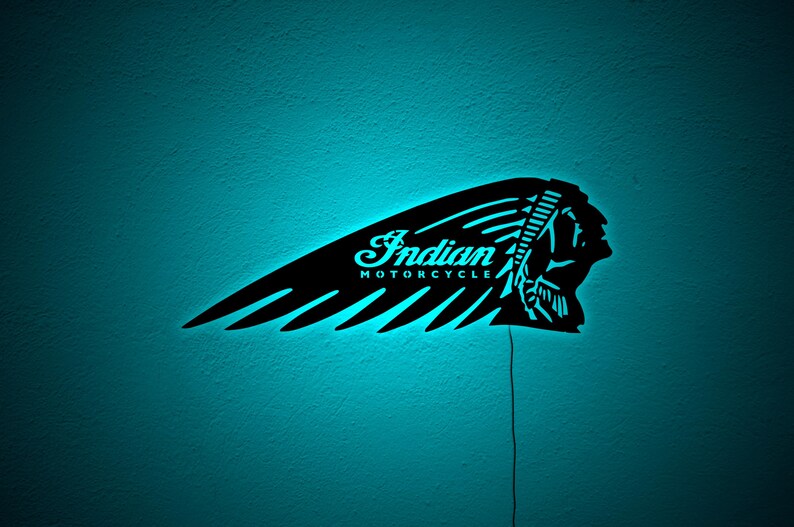 May include: Black Indian Motorcycle logo wall art with a turquoise neon glow. The logo features the text "Indian MOTORCYCLE" in a stylized font, along with the profile of a Native American chief. The wall art is mounted on a turquoise wall.