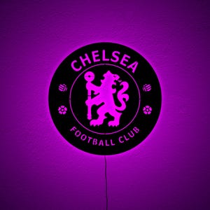 Puede incluir: Un letrero redondo negro del Chelsea Football Club con un resplandor p&uacute;rpura. El nombre y el emblema del club est&aacute;n en el centro, con un le&oacute;n p&uacute;rpura. El letrero est&aacute; iluminado con una luz p&uacute;rpura.