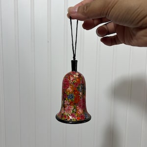 May include: A bell-shaped ornament with a black top and base, and a floral pattern in red, pink, orange, and blue. The ornament is suspended by a black string, suitable for hanging. The bell is likely a decorative item.