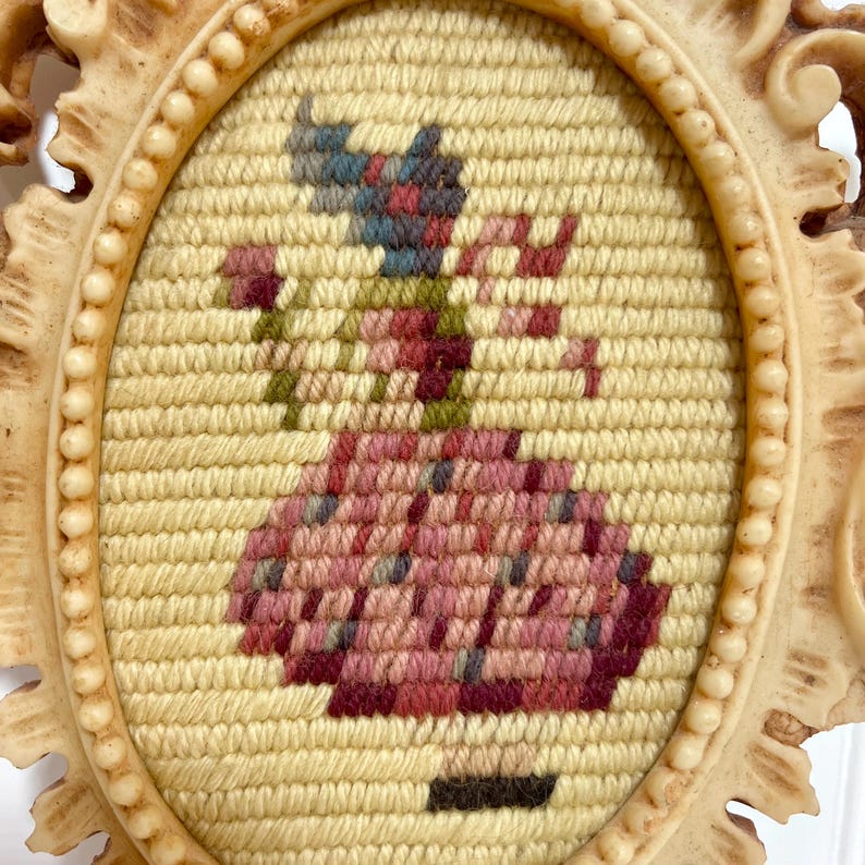 K&ouml;nnte beinhalten: Ovaler, cremefarbener Rahmen mit einem Gobelin-Design. Der Gobelin zeigt eine Figur in einem rosa Kleid, die eine Blume h&auml;lt, mit einem blauen und roten Hut. Der Rahmen hat einen Perlenrand und dekorative Kanten.