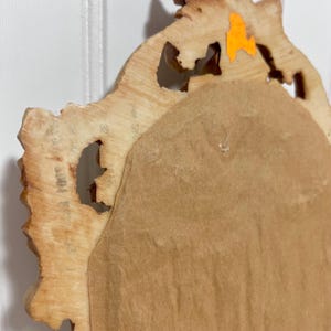 K&ouml;nnte beinhalten: R&uuml;ckseite eines dekorativen, verzierten Spiegels mit einem hellbraunen Holzrahmen. Der Rahmen hat ein geschnitztes, strukturiertes Design. Die Spiegelr&uuml;ckseite ist hellbraunes Papier. Ein orangefarbener Aufkleber ist auf dem Rahmen sichtbar.