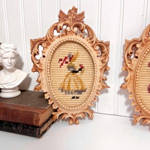 K&ouml;nnte beinhalten: Zwei ovale Vintage-Wandbeh&auml;nge mit verzierten, hellbraunen Rahmen. Jedes zeigt ein Gobelin-Design einer Frau in einem gelben Kleid, die einen rot-wei&szlig;en Gegenstand h&auml;lt. Die Rahmen haben ein detailliertes, geschnitztes Design.
