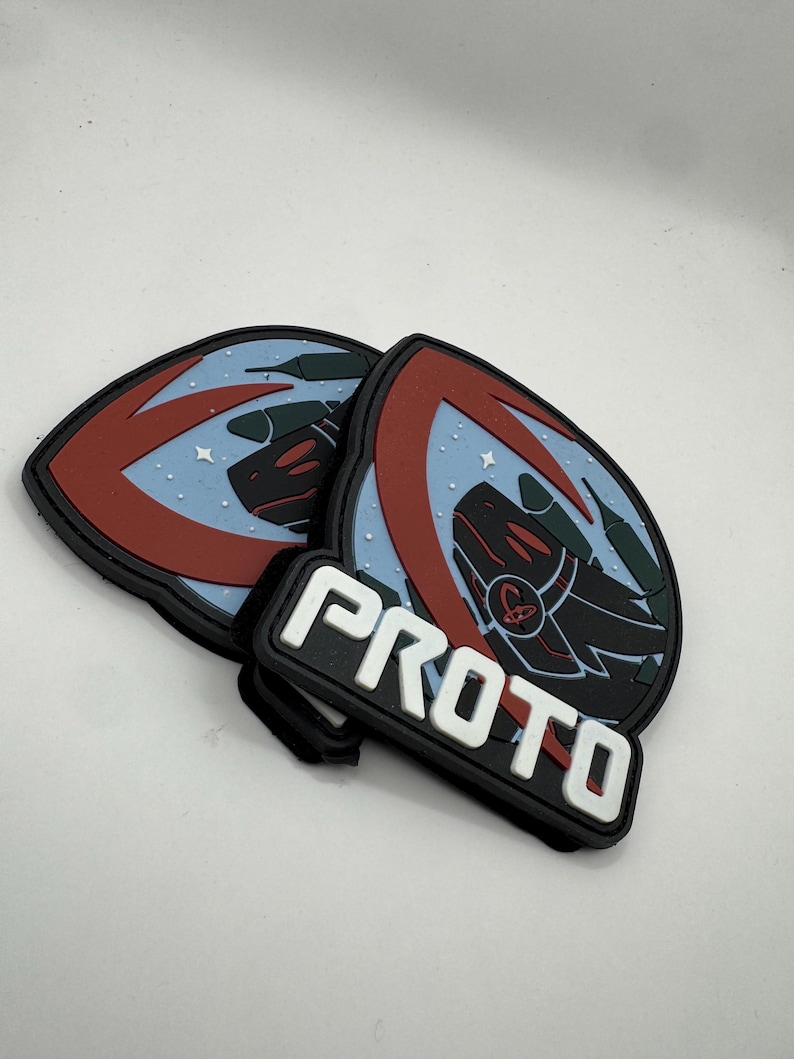 May include: A set of three black, red, and blue PVC patches. Two patches feature a stylized dragon design with a red arc and a light blue background. A rectangular patch below reads "PROTO" in white block letters.
