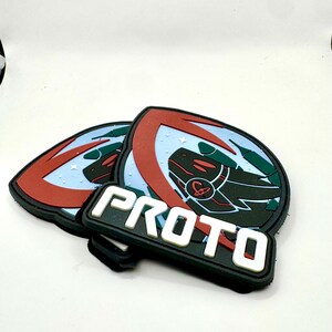 May include: Two black, red, and green PROT0 patches. The patches have a shield-like design with a red outline, a green and black graphic, and the word "PROTO" in white block letters.