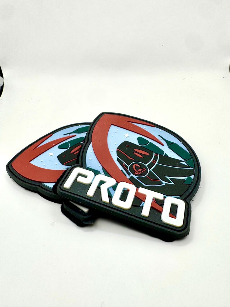 May include: Two black, red, and green PROT0 patches. The patches have a shield-like design with a red outline, a green and black graphic, and the word "PROTO" in white block letters.