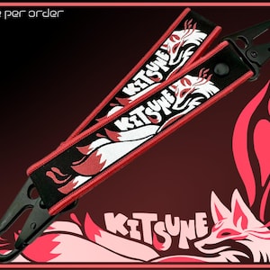 May include: Two black keychains with red trim and the word "KITSUNE" in white, featuring a fox design. The keychains have a black clasp and the text "one per order" is at the top. The background is a gradient of red and black.