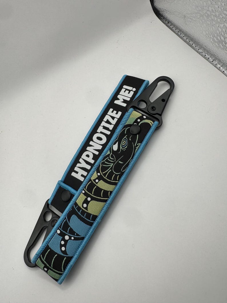 May include: A black and blue keychain wrist strap with the text "HYPNOTIZE ME!" in white. The strap features a black and green snake design. The strap has a black metal clasp.