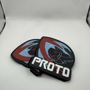May include: Two black, red, and blue PROTO patches. Each patch features a shield design with a dragon-like creature and the word "PROTO" in white block letters.