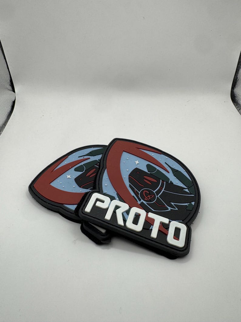 May include: Two black, red, and blue PROTO patches. Each patch features a shield design with a dragon-like creature and the word "PROTO" in white block letters.