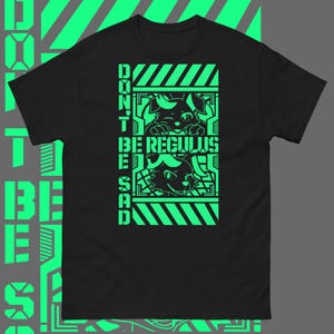 以下が含まれることがあります： 緑色のグラフィックデザインが施された黒いTシャツ。グラフィックには、スタイリッシュなフォントで「Don't Be Regulus Be Sad」というテキストが書かれた2匹の漫画の動物が描かれています。