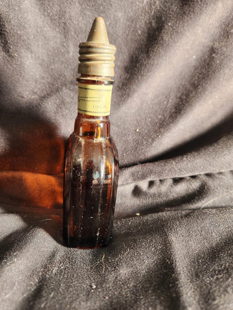 Pu&ograve; includere: Una piccola bottiglia di vetro marrone con un design a coste. La bottiglia ha un tappo di metallo e un'etichetta che recita "1.5 fl oz". La bottiglia &egrave; probabilmente per profumo o un liquido simile.
