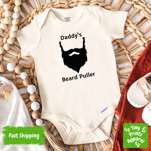 May include: A white baby onesie with a black silhouette of a beard and the text "Daddy's Beard Puller".