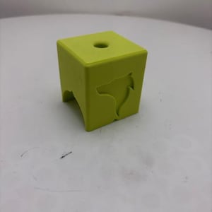May include: A lime green, cube-shaped object with a hole on top and a wolf head cutout on one side. The object has a minimalist design and is likely a decorative item or a small stool.