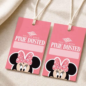 May include: Two rectangular pink gift tags with white string loops. Each tag features a graphic of a cartoon mouse with a pink bow, the text "YOU'VE BEEN PIXIE DUSTED" in white, and a blank rectangular space for writing names or messages.
