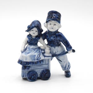 Figura de pareja de niños con carretilla de mano de porcelana de Rauenstein marcada Delft alrededor de 1900
