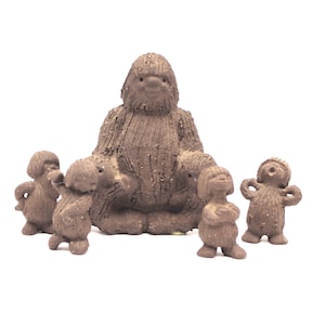 May include: A set of five brown, textured clay figurines featuring one large central figure sitting in a cross-legged position surrounded by four smaller standing figures, all with simple facial features and a rough, bark-like surface finish.