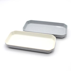 May include: Two rectangular trays. One is light gray, the other is off-white. Both have a slightly textured appearance and a subtle, scalloped edge design. The trays are likely for serving or organizing small items.