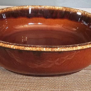 Könnte beinhalten: Eine braune und beige glasierte Keramik-Backform mit zwei Griffen. Die Form ist oval und hat eine braune Glasur mit einem beigefarbenen Rand.