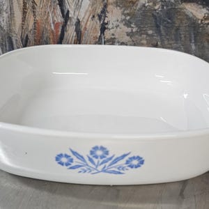 Może przedstawiać: Owalne, białe naczynie do pieczenia z niebieskim kwiatowym wzorem. Naczynie ma dwa uchwyty i jest wykonane z ceramiki. Klasyczny element wyposażenia kuchni do pieczenia i serwowania.